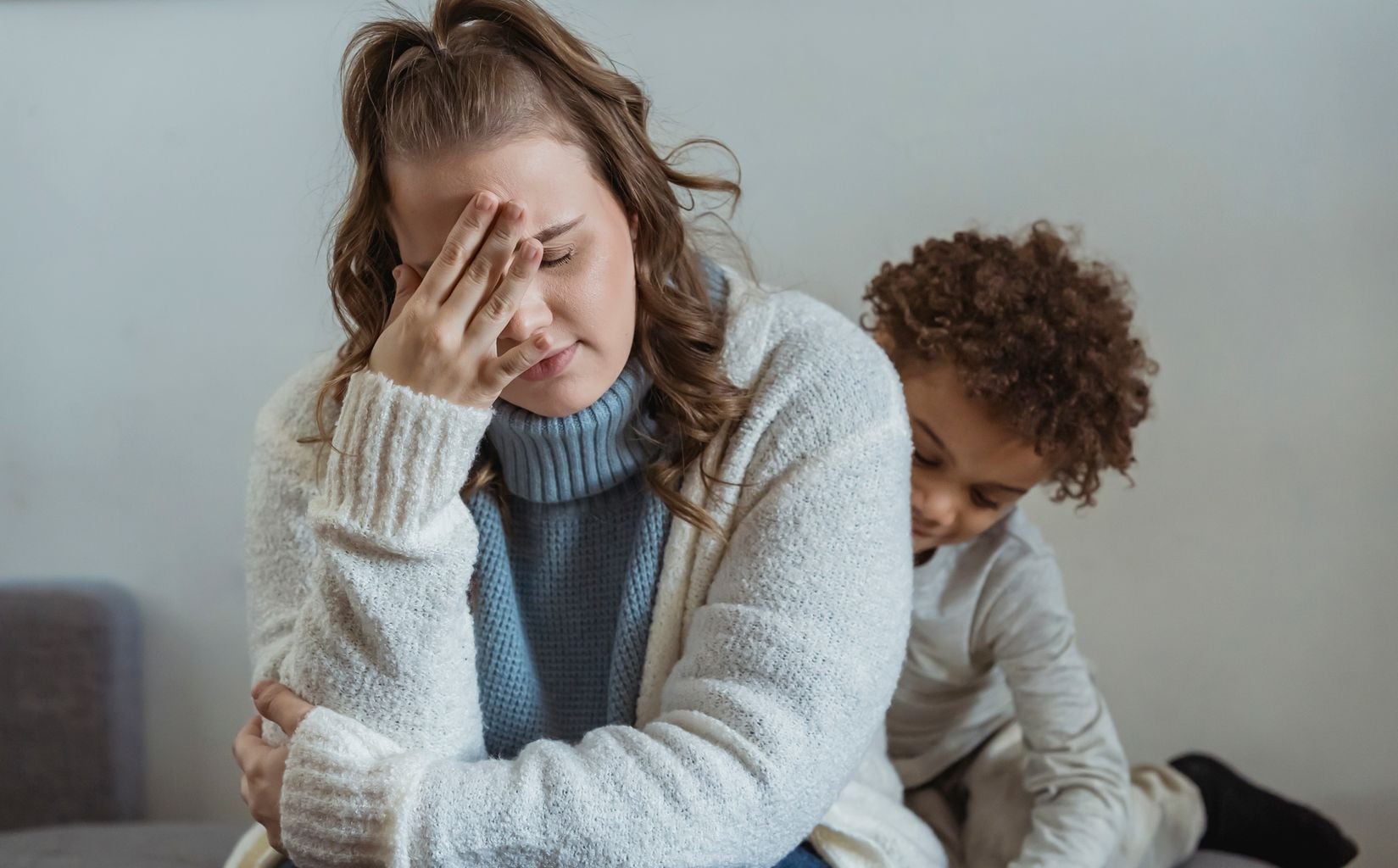 A frustrated, exhausted parent sitting with hand on forehead at home