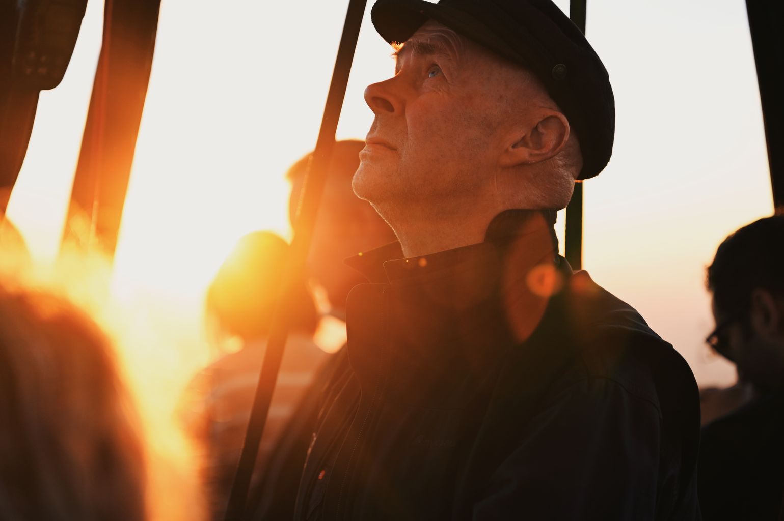 Profile of an elderly man in a hat gazing at a sunset with dramatic lighting