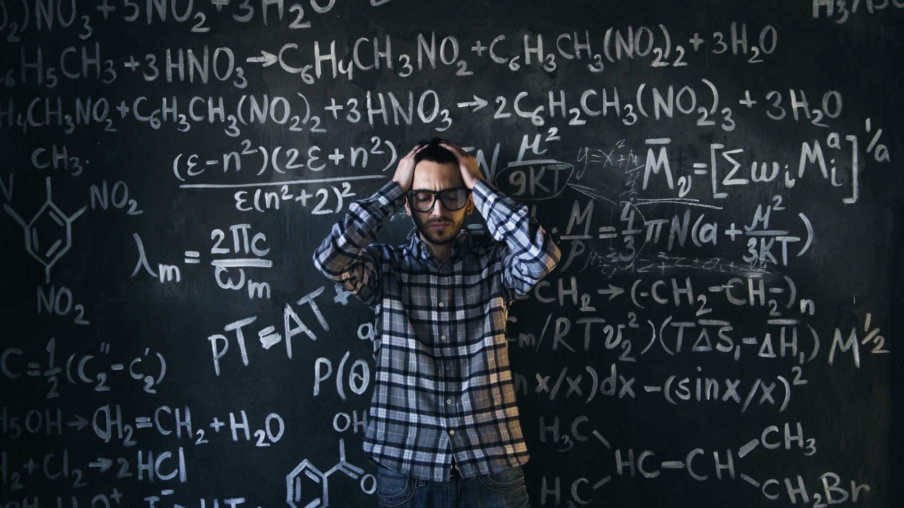 Man in glasses focusing on math problems on a chalkboard