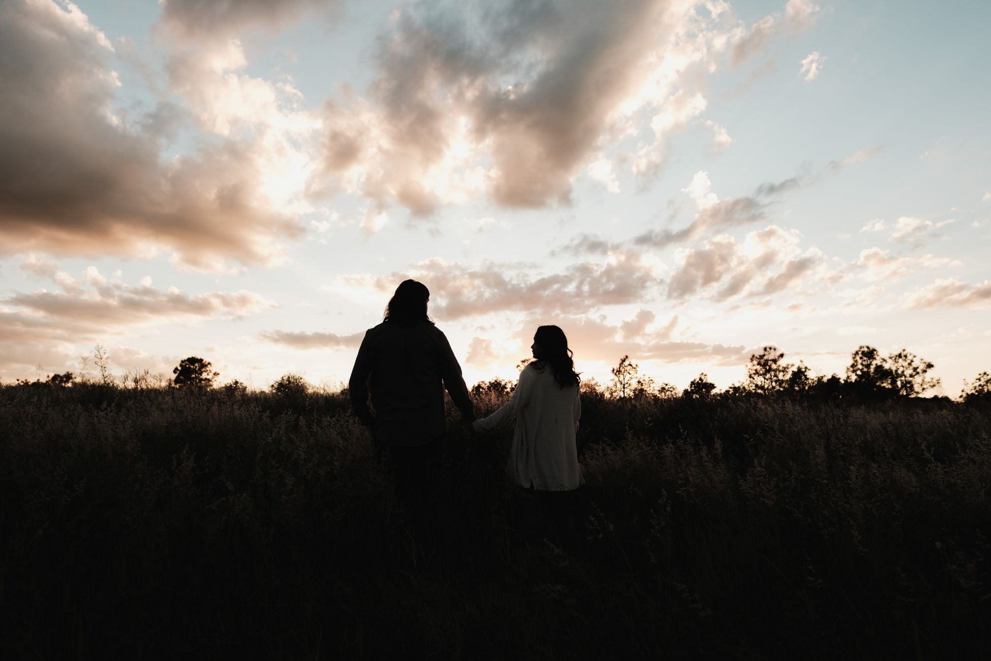 Silhouette of a couple holding hands while watching a beautiful sunset outdoors in a natural setting.