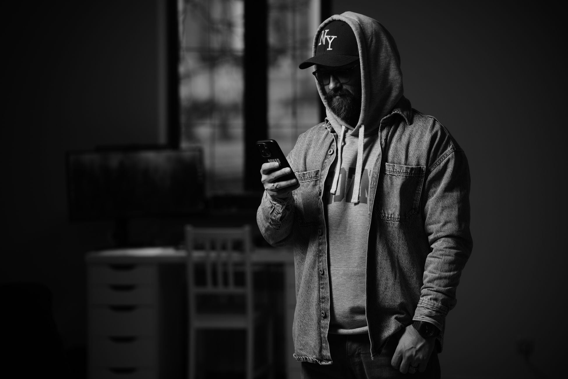 Bearded man in hoodie using smartphone in dark room, stylish and modern