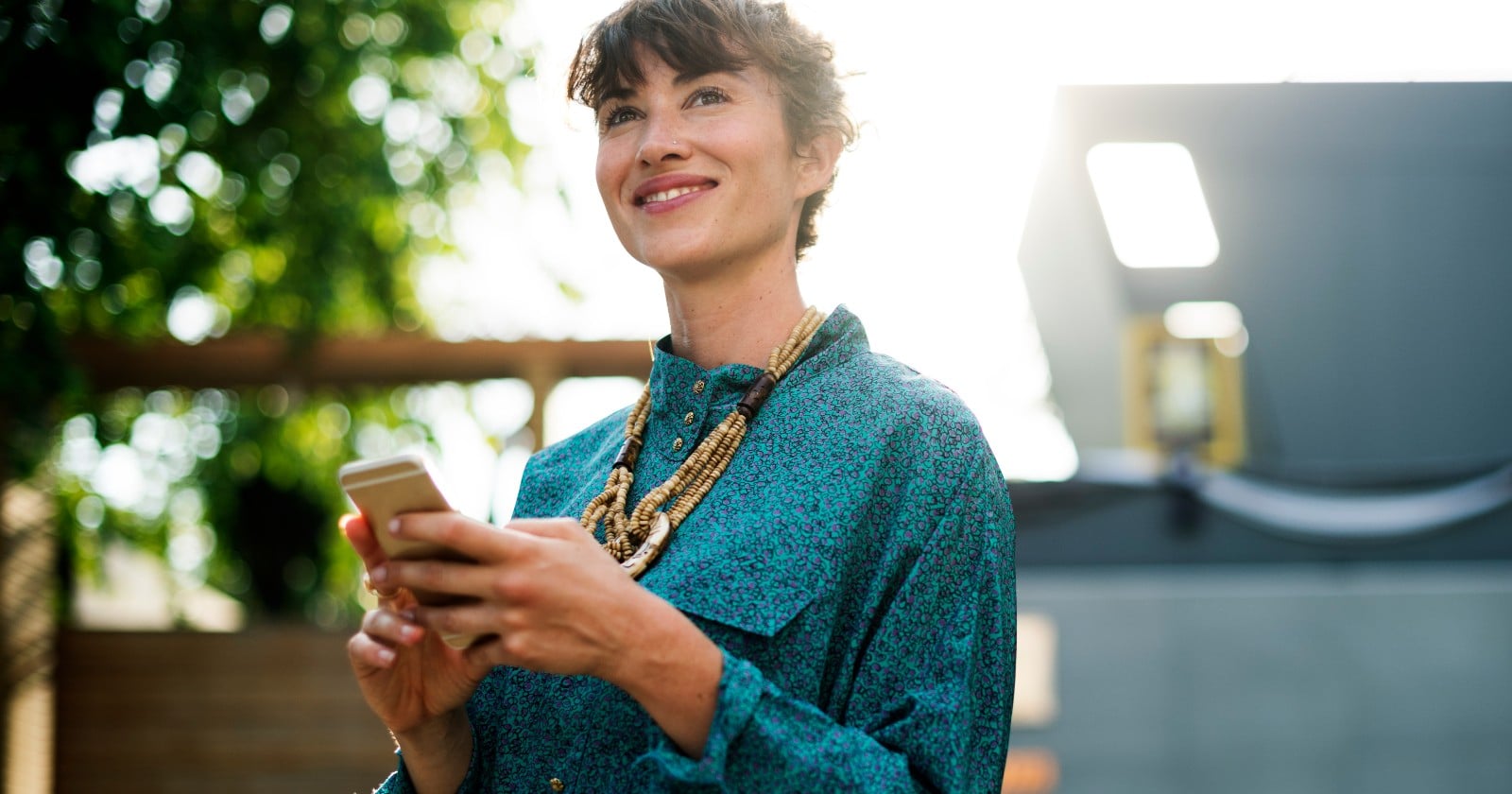 A smiling woman holding a mobile phone in warm daylight